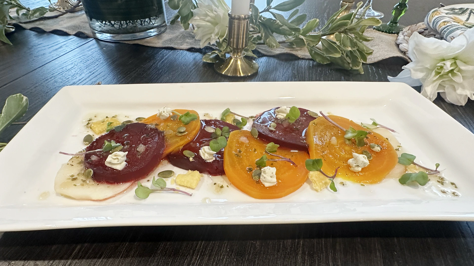 A plated appetizer of golden beet and red beet slices with crumbled cheese, microgreens, and creamy dressing on a white rectangular platter.